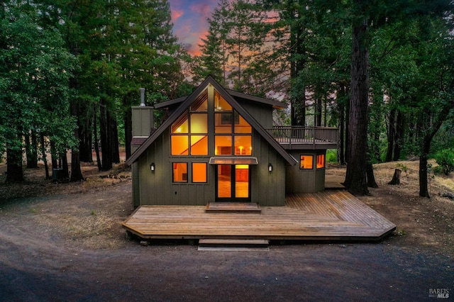 back of house at dusk featuring a chimney and a wooden deck