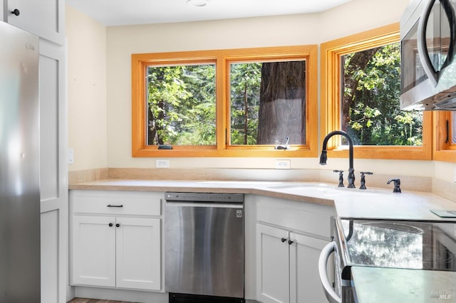 kitchen featuring stainless steel appliances, white cabinets, light countertops, and plenty of natural light