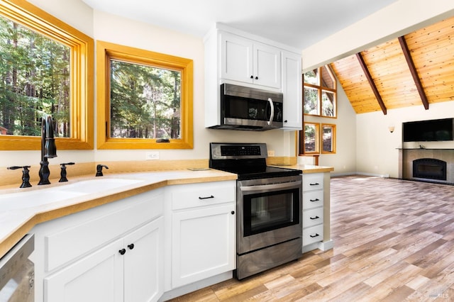 kitchen featuring lofted ceiling with beams, appliances with stainless steel finishes, open floor plan, a fireplace, and a sink