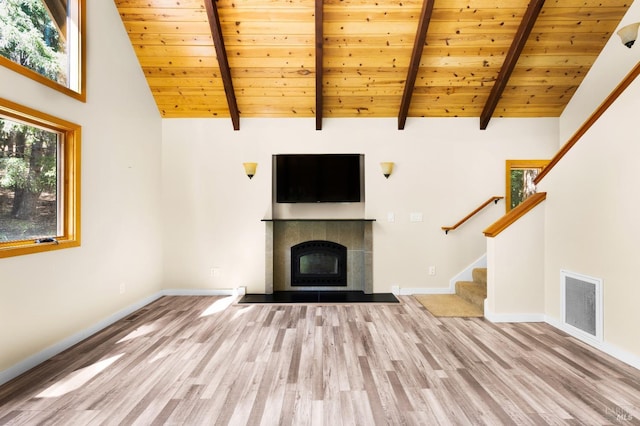 unfurnished living room featuring visible vents, a tiled fireplace, stairway, wood finished floors, and beamed ceiling