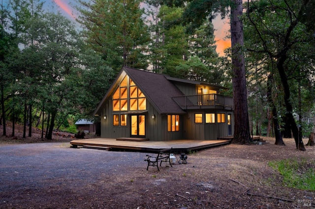 rear view of property featuring driveway, a shingled roof, a balcony, a wooden deck, and board and batten siding