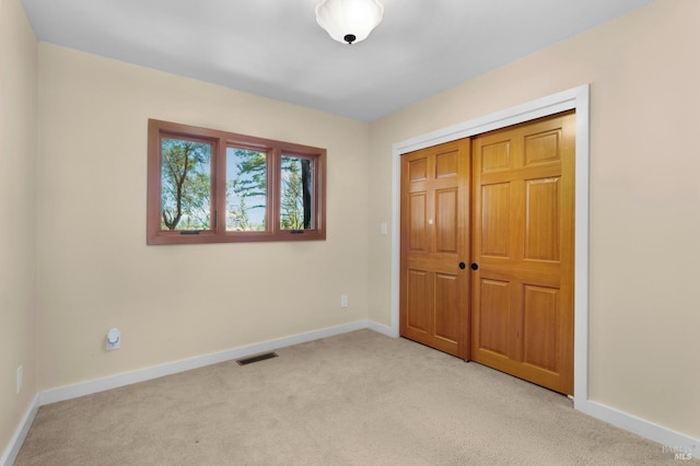 unfurnished bedroom featuring visible vents, baseboards, a closet, and light colored carpet