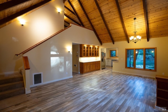 unfurnished living room with visible vents, stairway, an inviting chandelier, wood finished floors, and baseboards