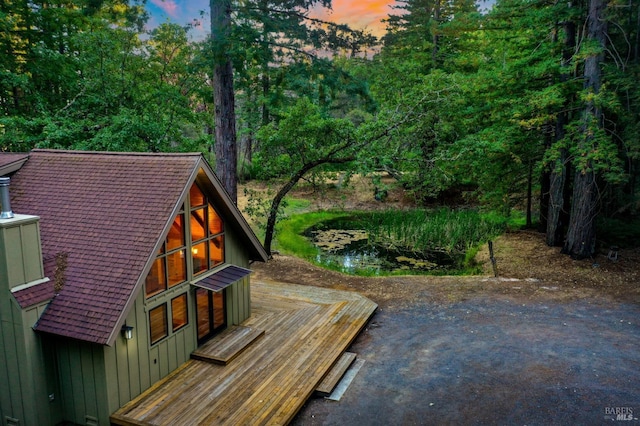 exterior space with board and batten siding, a shingled roof, and a forest view