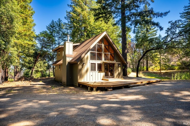 rear view of house with board and batten siding, a chimney, and a wooden deck