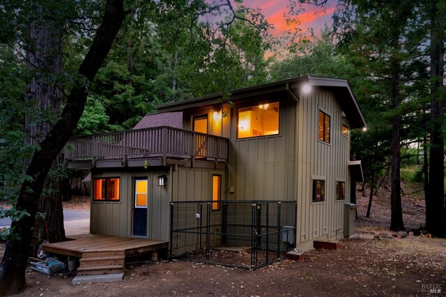 back house at dusk featuring a balcony and a wooden deck