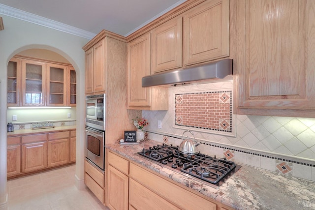 kitchen with ornamental molding, appliances with stainless steel finishes, light stone countertops, and light brown cabinets