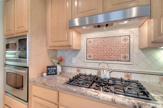 kitchen with light stone counters, stainless steel appliances, backsplash, and light brown cabinets