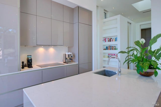 kitchen with modern cabinets, gray cabinetry, a sink, built in features, and black electric stovetop