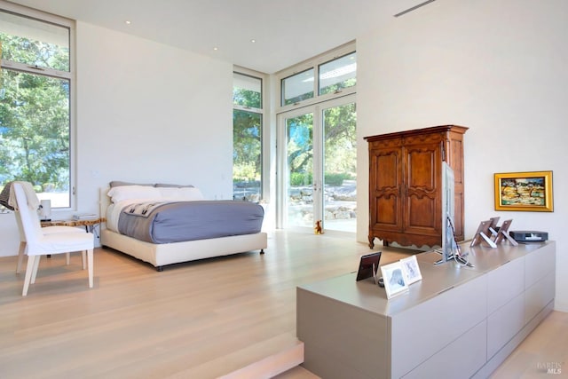 bedroom with access to exterior, a towering ceiling, floor to ceiling windows, and light wood finished floors