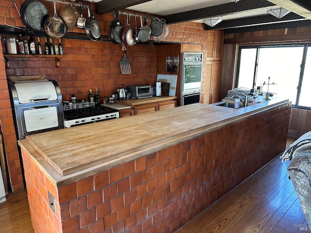 kitchen featuring beam ceiling, dark hardwood / wood-style flooring, and stainless steel double oven