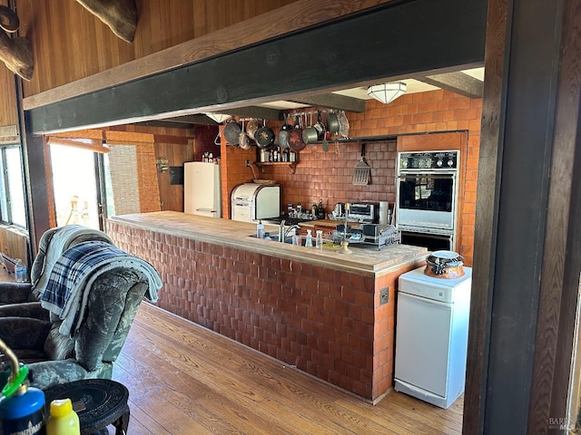 kitchen featuring brick wall, water heater, hardwood / wood-style floors, and double oven