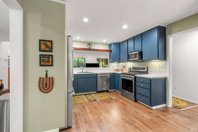 kitchen with blue cabinetry, stainless steel appliances, light countertops, light wood-style floors, and a sink