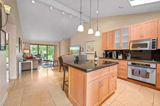 kitchen featuring light brown cabinets, a kitchen breakfast bar, appliances with stainless steel finishes, a center island, and glass insert cabinets