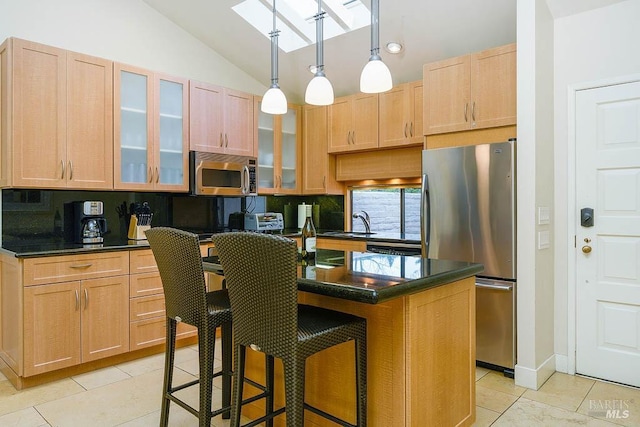 kitchen featuring a breakfast bar area, stainless steel appliances, a center island, light brown cabinetry, and decorative light fixtures