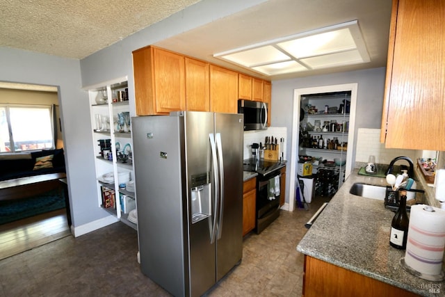 kitchen with a textured ceiling, stone countertops, stainless steel appliances, a sink, and backsplash