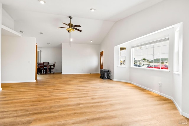 empty room featuring ceiling fan, lofted ceiling, a wood stove, and light wood-type flooring