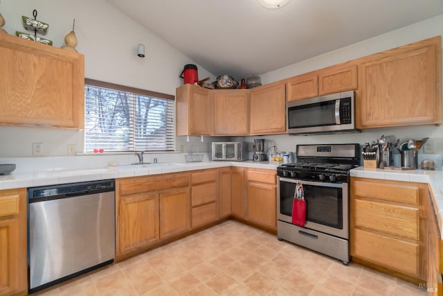 kitchen featuring tile countertops, sink, stainless steel appliances, and lofted ceiling