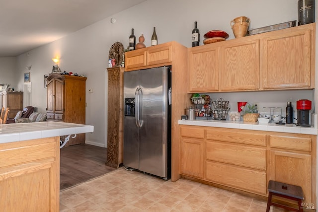 kitchen featuring tile counters, stainless steel fridge with ice dispenser, light brown cabinetry, and light hardwood / wood-style flooring