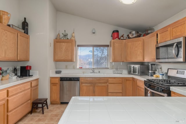 kitchen featuring appliances with stainless steel finishes, light brown cabinetry, vaulted ceiling, sink, and tile counters