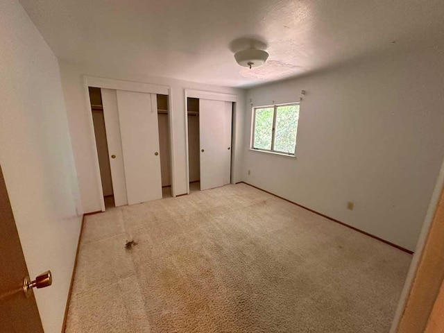 unfurnished bedroom featuring light carpet and multiple closets