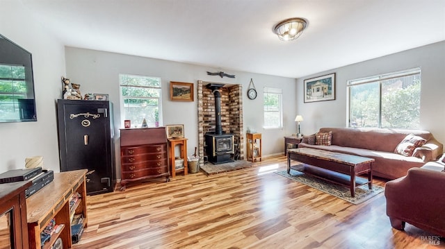 living room with a wood stove, brick wall, a wealth of natural light, and light hardwood / wood-style floors