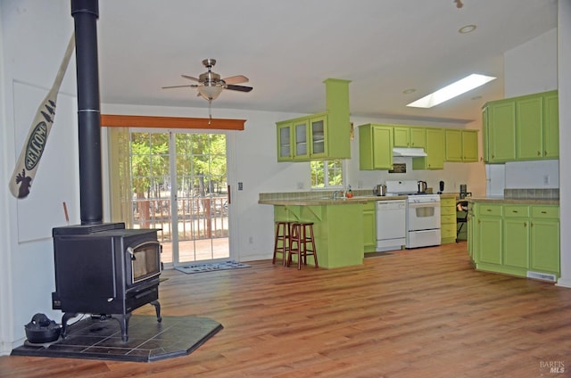 kitchen featuring white appliances, light wood-type flooring, lofted ceiling with skylight, and a wood stove