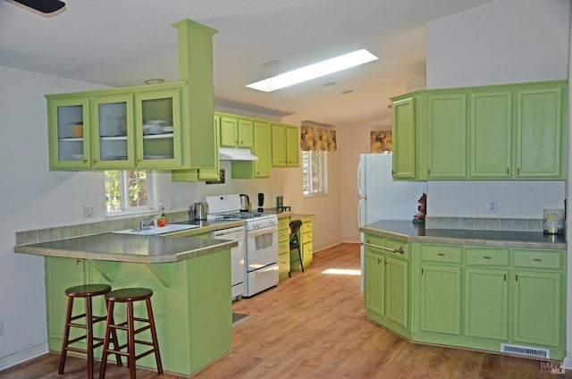 kitchen featuring sink, gas range gas stove, a kitchen breakfast bar, kitchen peninsula, and green cabinets