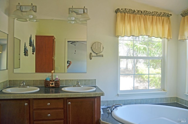 bathroom featuring dual bowl vanity, a bath, and a healthy amount of sunlight