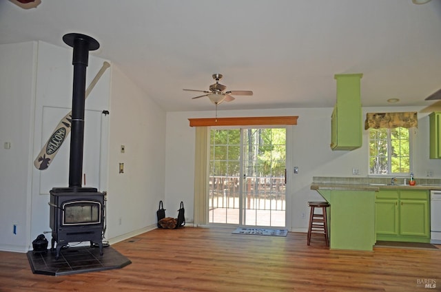 living room featuring ceiling fan, a wood stove, sink, and hardwood / wood-style flooring