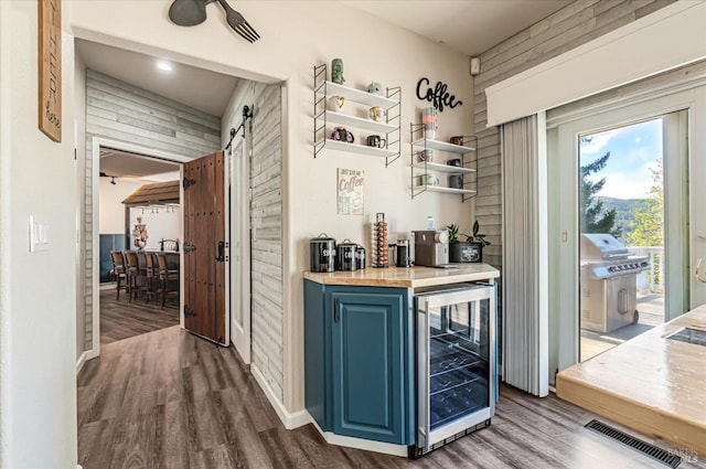 bar with blue cabinets, wine cooler, a barn door, wooden counters, and hardwood / wood-style floors