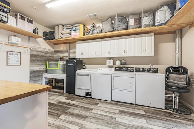 washroom featuring a textured ceiling, light hardwood / wood-style floors, independent washer and dryer, and cabinets