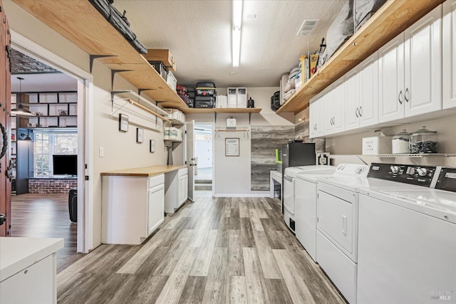 laundry area featuring light wood-type flooring, washer and clothes dryer, a textured ceiling, and cabinets