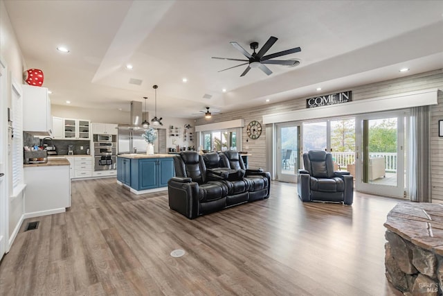 living room featuring a tray ceiling, light hardwood / wood-style floors, ceiling fan, and sink