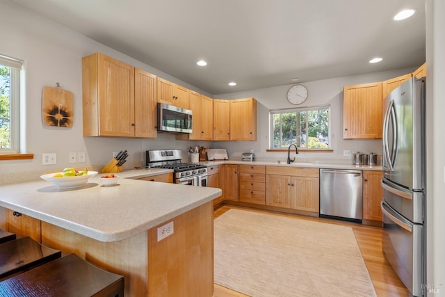 kitchen with light wood-type flooring, a kitchen breakfast bar, stainless steel appliances, sink, and kitchen peninsula