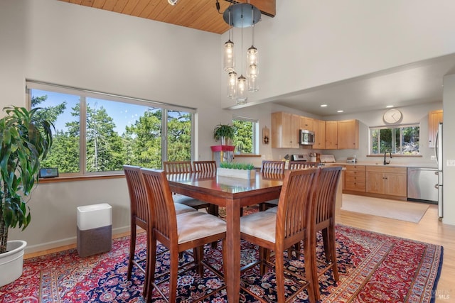 dining area with sink, light wood-type flooring, a chandelier, and a high ceiling