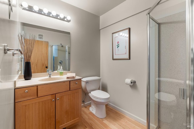 bathroom featuring vanity, toilet, wood finished floors, a stall shower, and baseboards