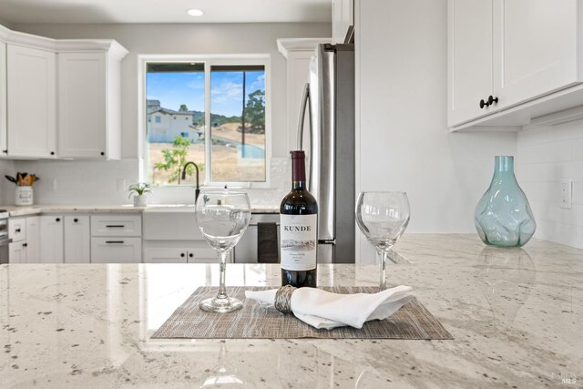 kitchen featuring light stone countertops, stainless steel fridge, and white cabinetry