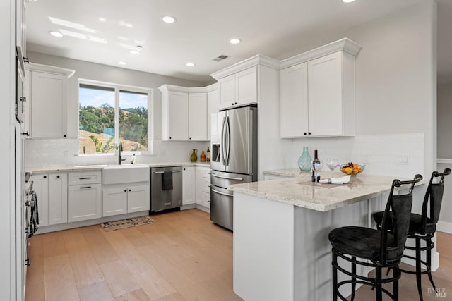 kitchen with kitchen peninsula, appliances with stainless steel finishes, sink, light hardwood / wood-style flooring, and white cabinetry