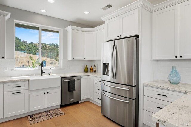 kitchen with light stone countertops, stainless steel appliances, backsplash, white cabinets, and light wood-type flooring