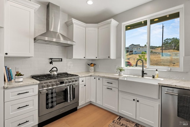 kitchen with white cabinetry, sink, wall chimney range hood, light hardwood / wood-style flooring, and appliances with stainless steel finishes