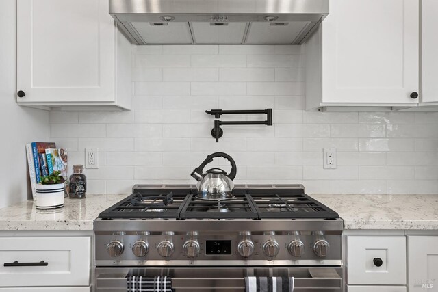 kitchen featuring exhaust hood, high end stainless steel range oven, light stone countertops, tasteful backsplash, and white cabinetry