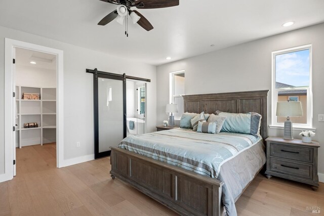 bedroom featuring a walk in closet, ceiling fan, light hardwood / wood-style flooring, and a barn door