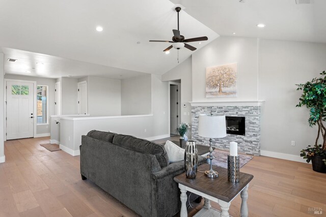 living room featuring lofted ceiling, ceiling fan, a stone fireplace, and light wood-type flooring