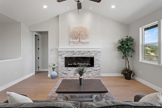 living room with a stone fireplace, ceiling fan, light hardwood / wood-style flooring, and lofted ceiling