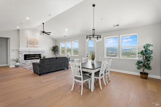 dining room featuring ceiling fan with notable chandelier, light hardwood / wood-style floors, lofted ceiling, and a fireplace