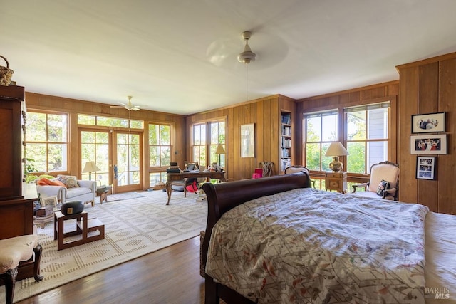 bedroom with ceiling fan, wood walls, french doors, and light hardwood / wood-style floors