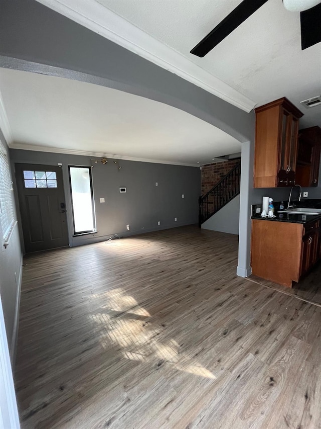 unfurnished living room featuring stairs, ornamental molding, wood finished floors, and a sink