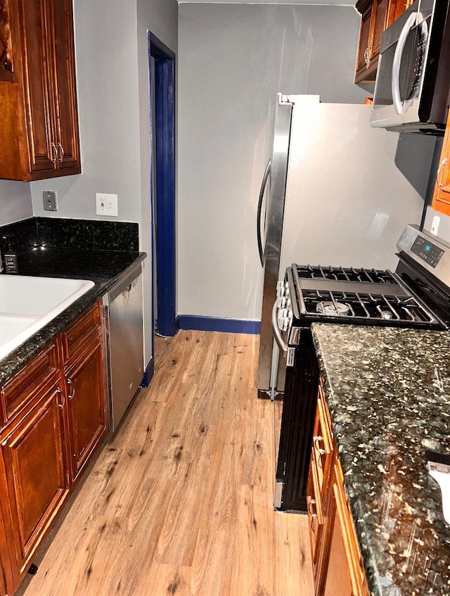 kitchen with a sink, baseboards, light wood-style floors, appliances with stainless steel finishes, and dark stone countertops