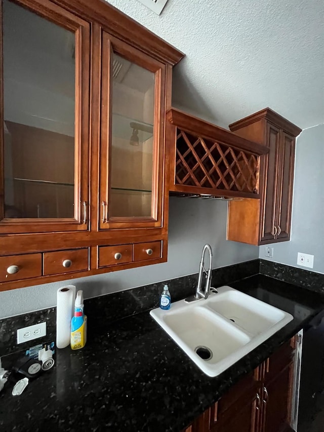 kitchen with glass insert cabinets, a sink, a textured ceiling, and dark stone countertops